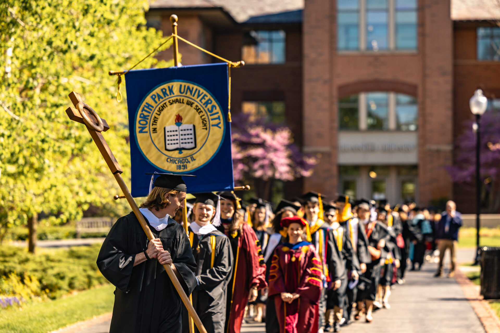Students at commencement outdoors, holding a banner in front of Brandel Library