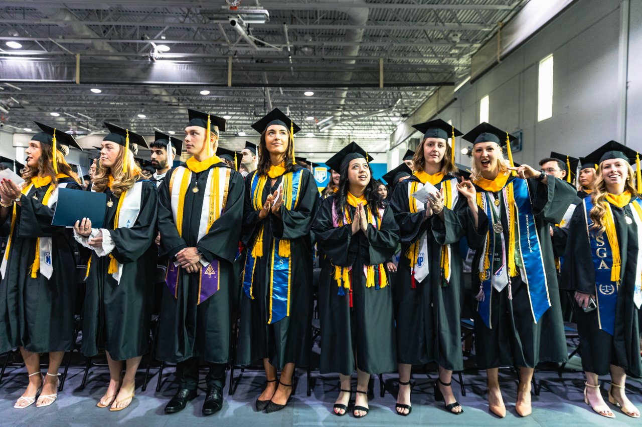 A group of graduates stands and applauds themselves.