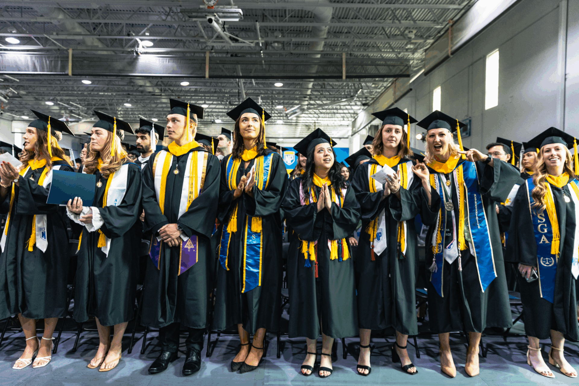 A group of graduates stands and applauds themselves.