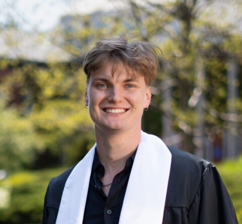 Student standing outside with black commencement robes and white stole.