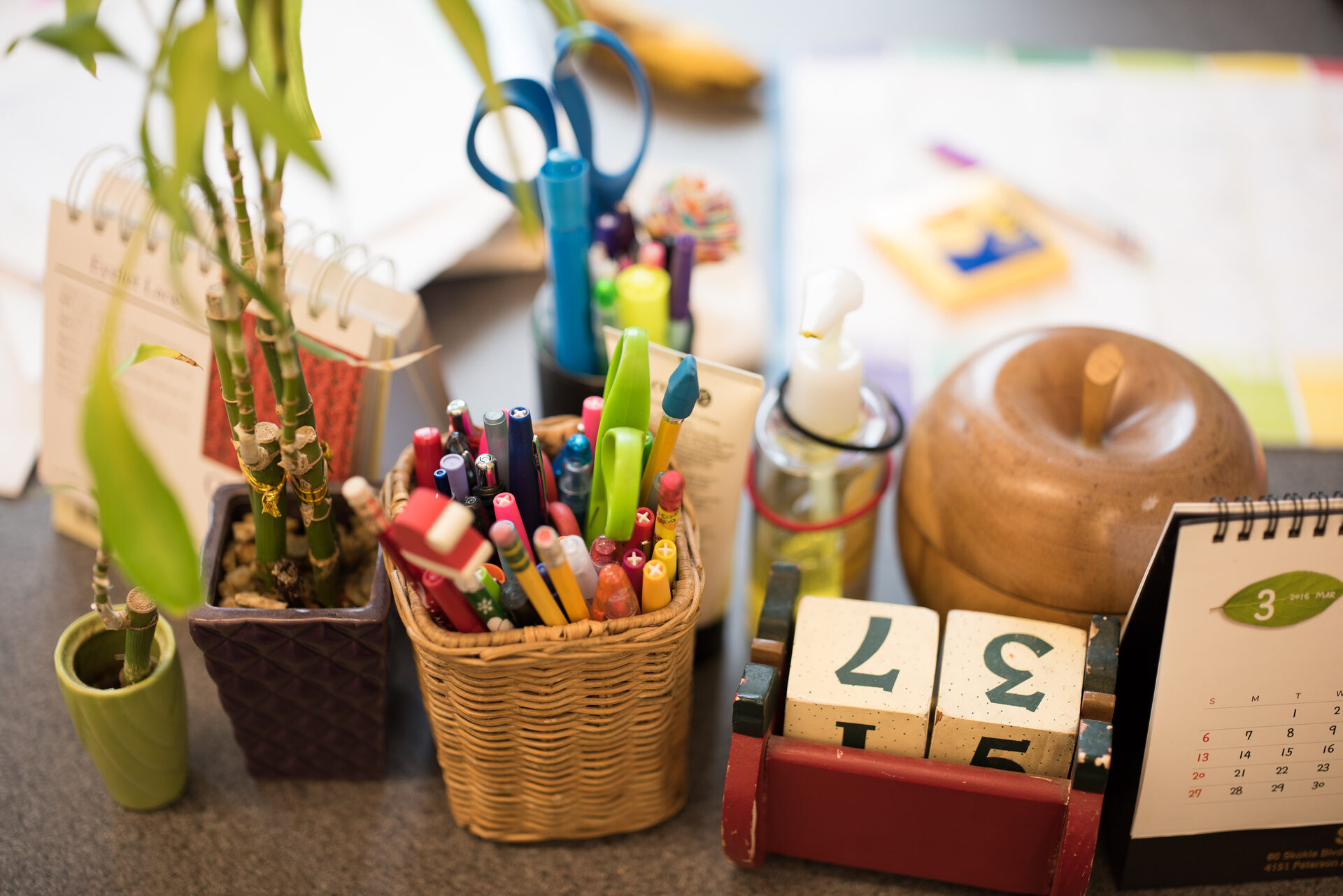 Pencil holder, plant, and wooden block calendar sit on top of an educator's desk