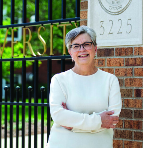 Woman standing outdoors against a brick wall and metal gate.